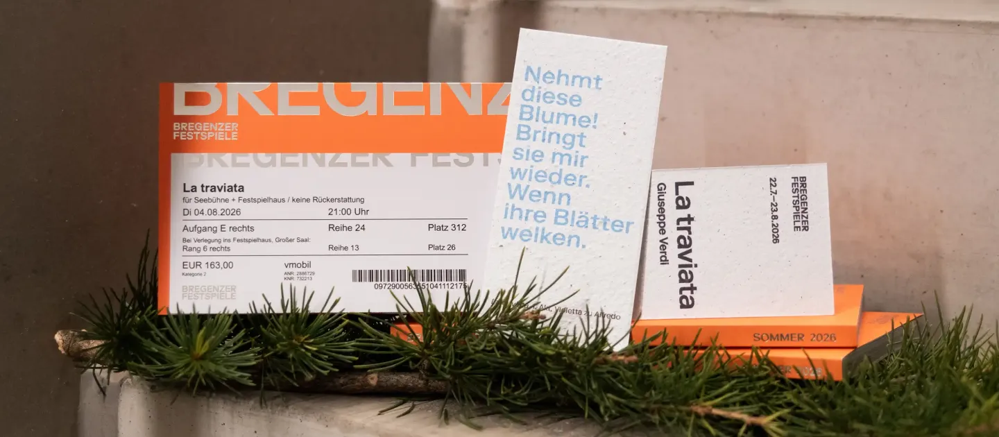 Mehrere Eintrittskarten für die Bregenzer Festspiele 2026 liegen auf einer Treppenstufe, davor Tannenzweige. Eine Karte trägt den Titel 'La traviata'.