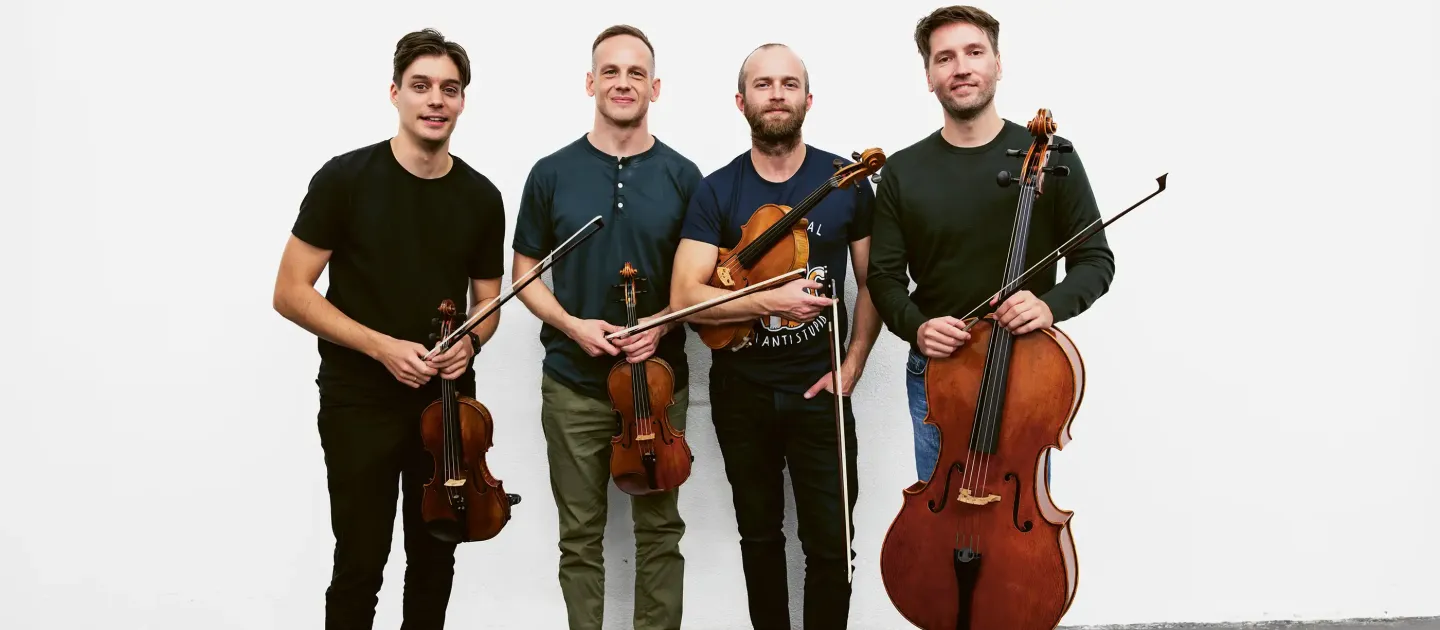 Vier Männer stehen nebeneinander und halten Streichinstrumente, zwei Geigen, eine Bratsche und ein Cello.