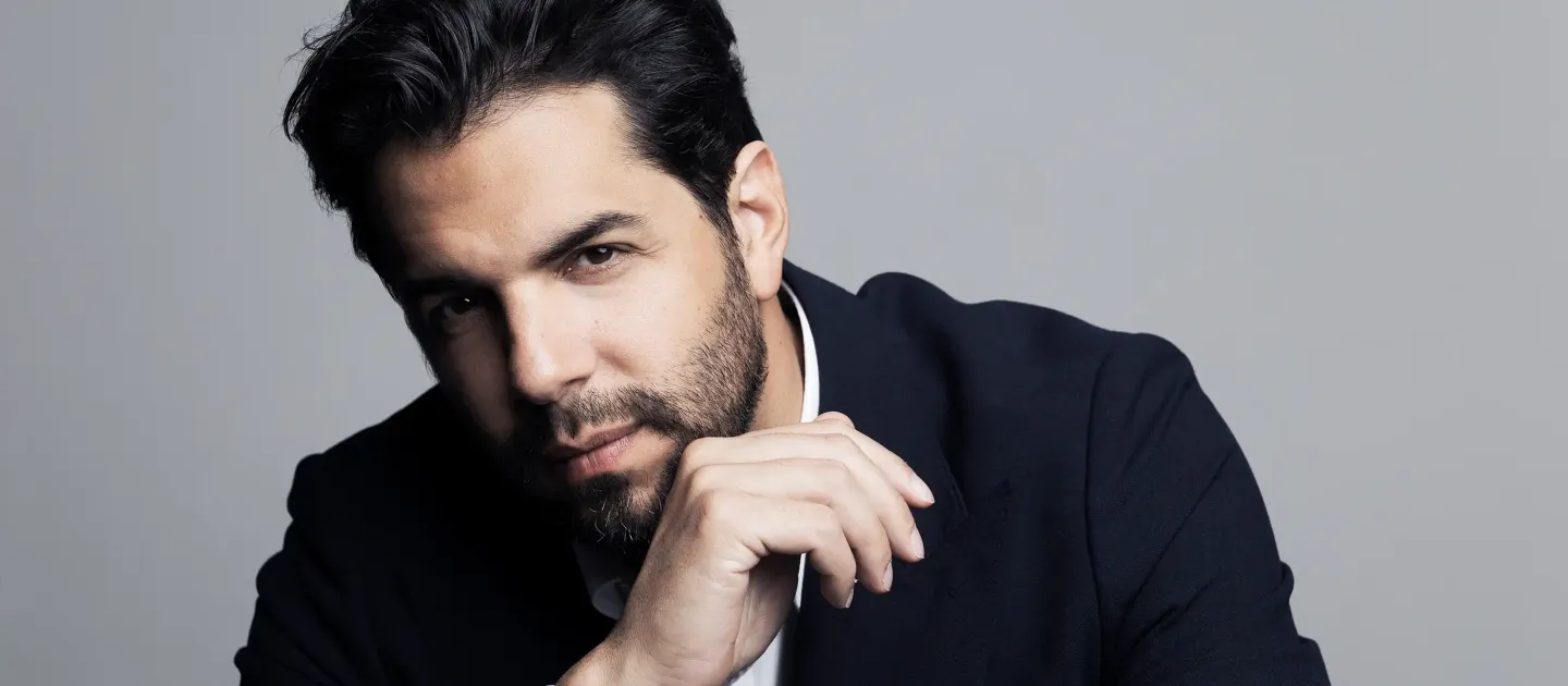 Domingo Hindoyan © Benjamin Ealovega Mann mit dunklem Haar und Bart stützt das Kinn auf die Hand und blickt in die Kamera