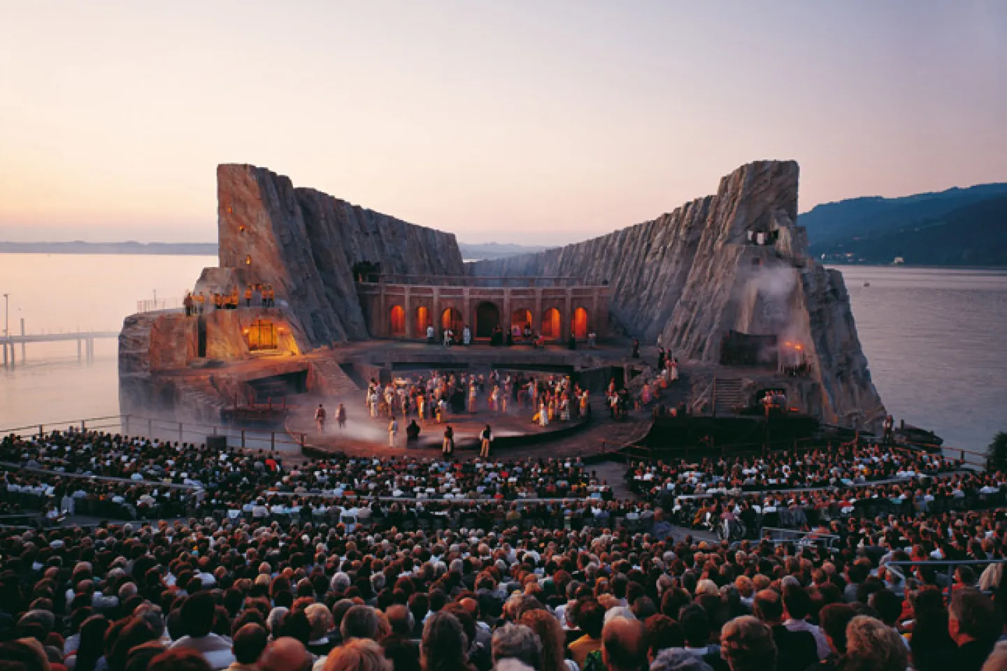 © Bregenzer Festspiele Szene aus "Carmen", 1991 auf der Seebühne, zweistöckiges Bühnenbild, Felsenlandschaft, seitlich hohe Felsen, mittig ein verbindender Gang, untere Ebene mit mehreren kostümierten Darstellenden