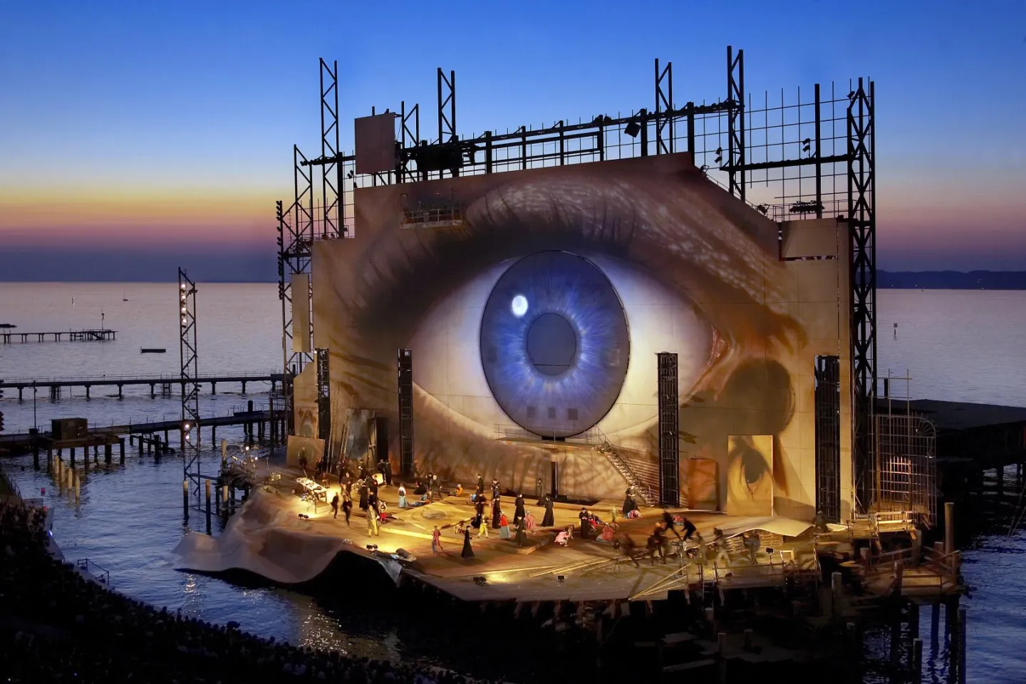 © Bregenzer Festspiele / andereart Szene aus "Tosca", 2007 auf der Seebühne, großes, flächendeckendes Auge auf der Rückwand, kostümierte Darstellende auf der Bühne