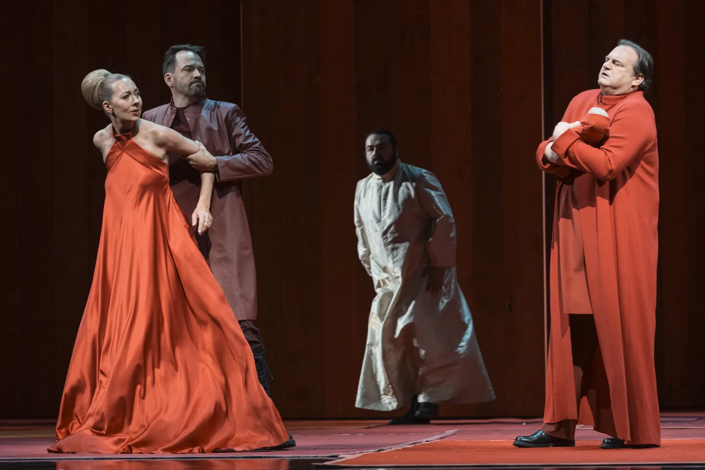 Szene aus "Œdipe", 2025 im Festspielhaus, links Jokaste (Marina Prudenskaya) im roten Kleid, von Créon (Tuomas Pursio) an den Armen gehalten, im Hintergrund Le Grand Prêtre (Nika Guliashvili) im hellen Gewand, rechts Laïos (Michael Heim) mit Baby Œdipe im Arm
