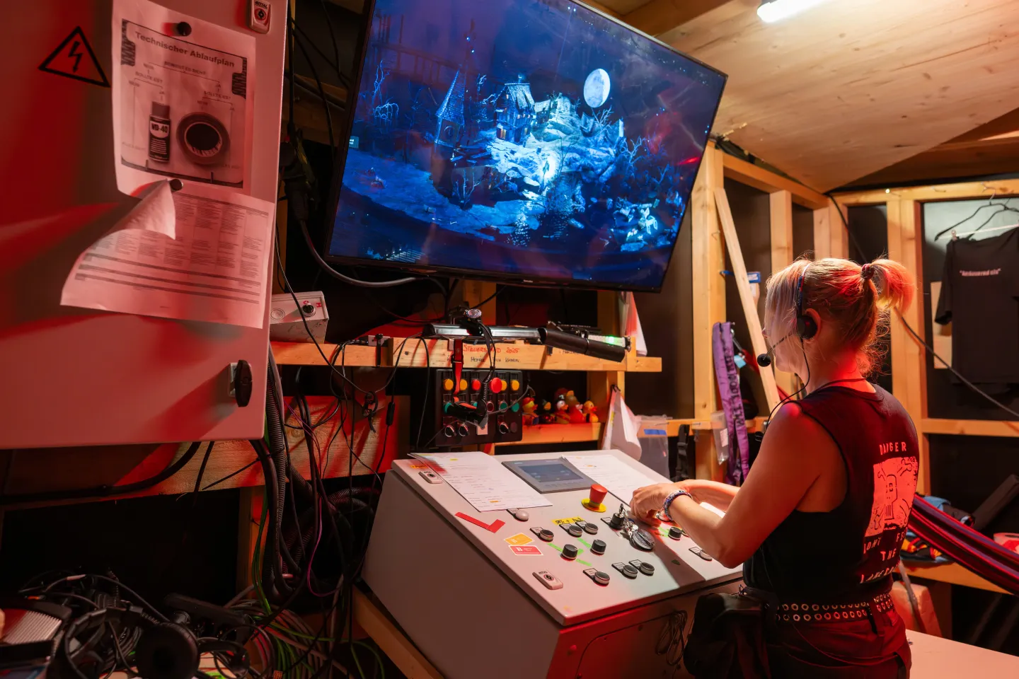 © Bregenzer Festspiele / Christian Lins Person bedient Steuerpult mit Monitor, der eine nächtliche Bühnenkulisse mit Mond zeigt, im Backstage-Bereich einer Theaterproduktion