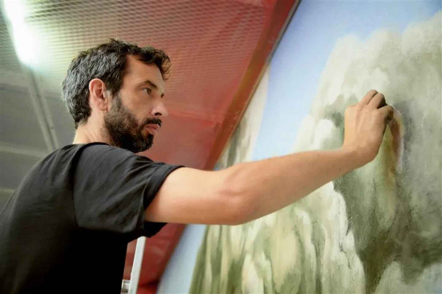 Nicolas Party © Woojeong Lee Person mit schwarzem T-Shirt arbeitet an einer großflächigen Wandmalerei mit grünen und weißen Farbtönen.