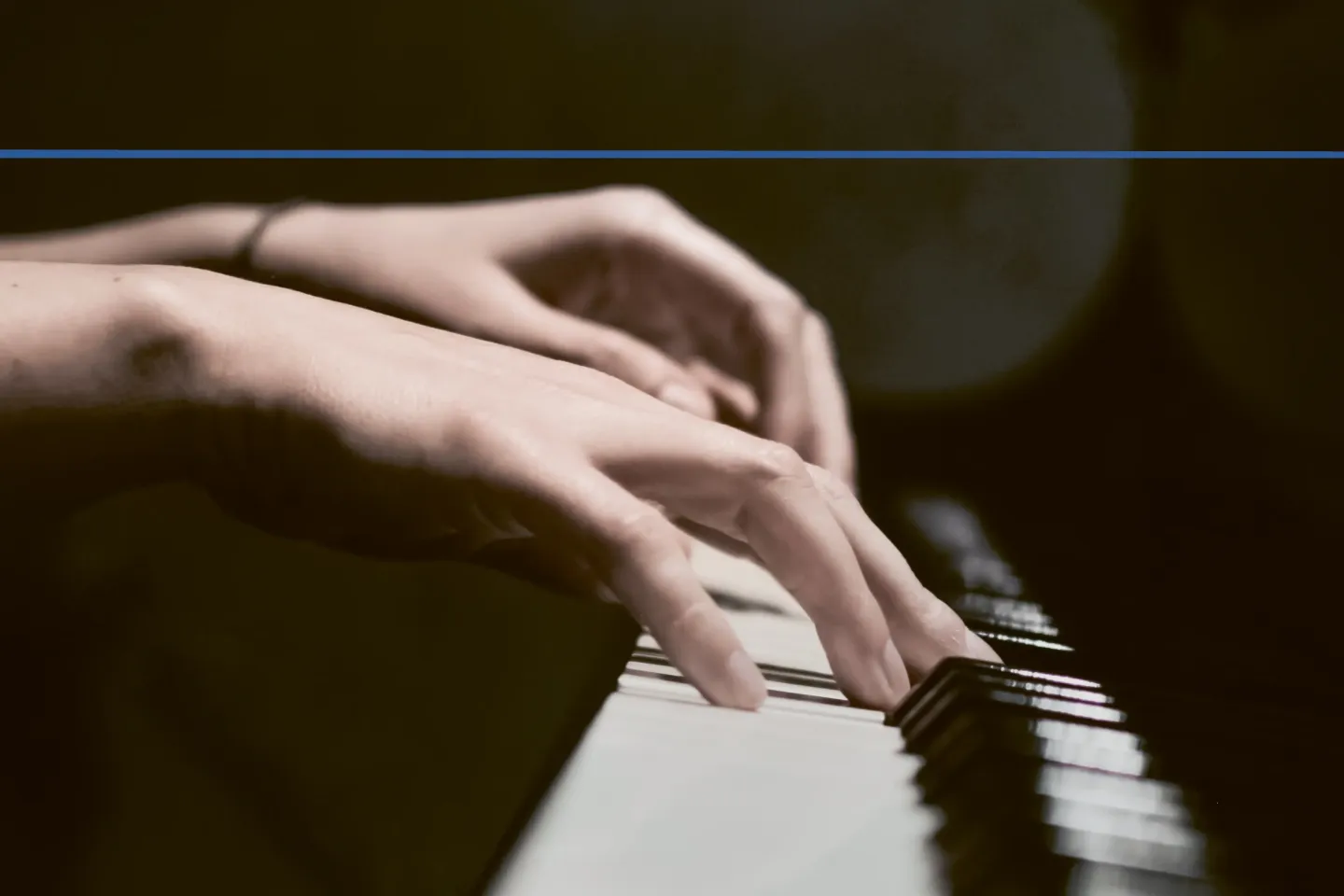 Detailaufnahme von Händen an einem Klavier mit dunklem Hintergrund
