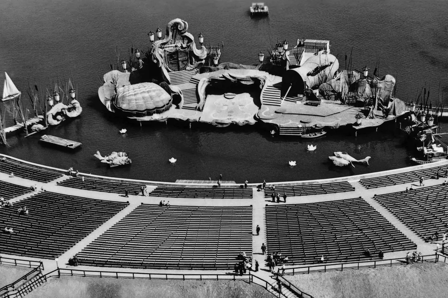 Schwarz-weiße Luftaufnahme eines Freilichttheaters mit Wasserbühne und mehreren Sitzreihen