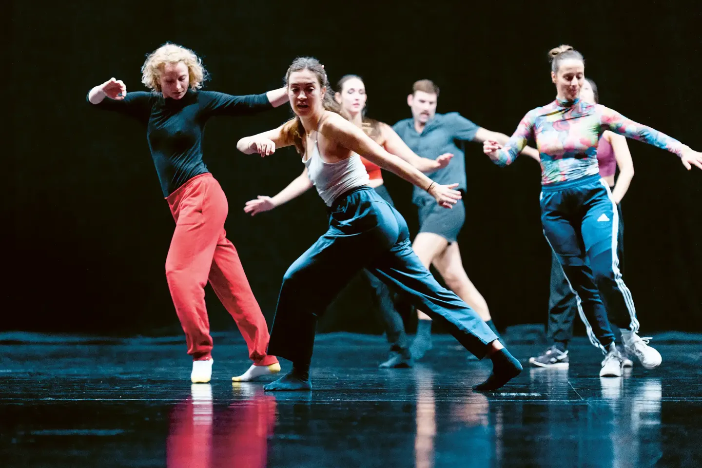 © Bregenzer Festspiele / Anja Koehler Gruppe von Tänzerinnen und Tänzern in sportlicher Kleidung in dynamischer Pose auf einer Bühne mit dunklem Hintergrund