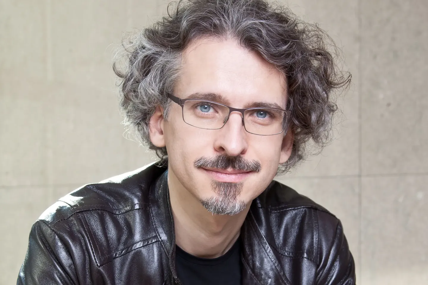 Bernd Richard Deutsch © Stefanie Luger Person mit lockigem Haar und schwarzer Lederjacke vor einer Betonwand
