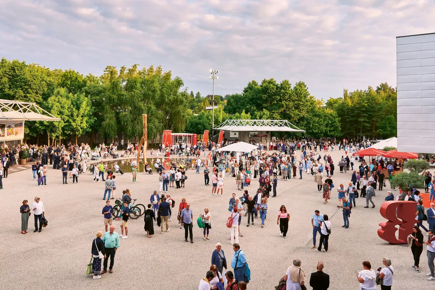 © Bregenzer Festspiele / Anja Koehler Große Menschenmenge auf Festspielplatz mit Bäumen im Hintergrund. und teilweise bewölktem Himmel