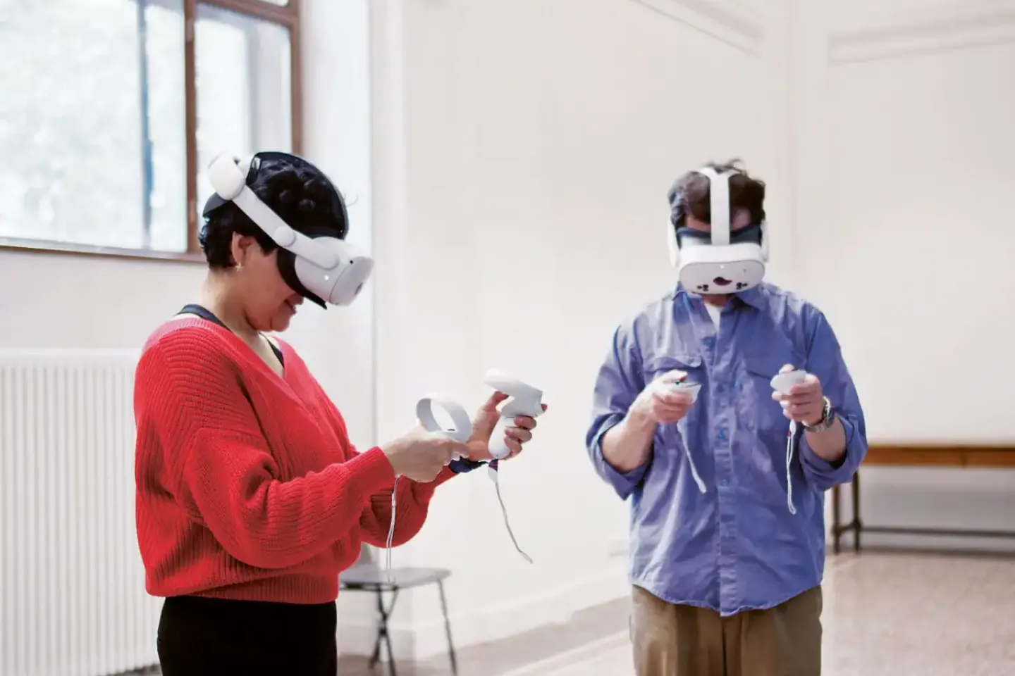 Zwei Personen mit VR-Brillen und Controllern in einem hellen Raum mit großen Fenstern