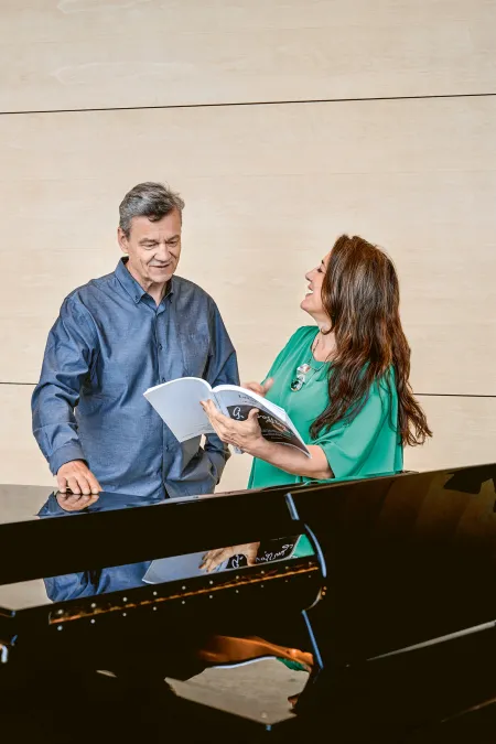 Lilli Paasikivi und Jaakko Kortekangas stehen am Flügel, sie hält ein Notenbuch und lächelt ihn an, er schaut darauf