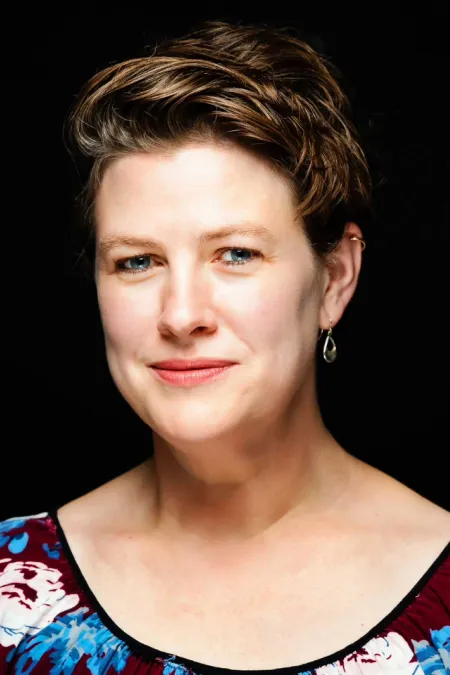 Portrait der Regisseurin Amy Lange vor schwarzem Hintergrund, kurze Haare, lächelnd