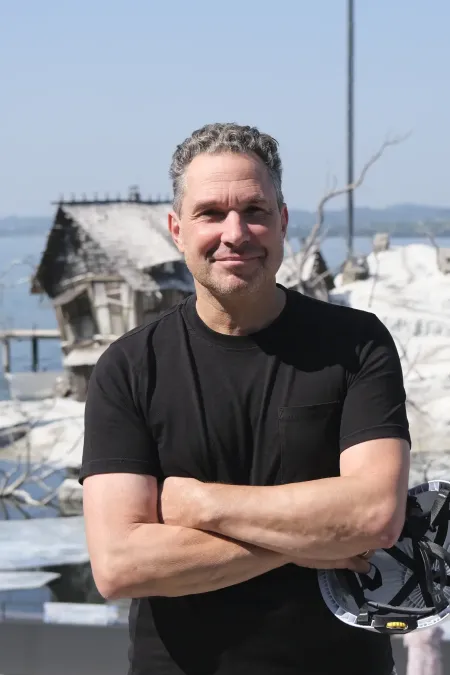 Mann mit verschränkten Armen und schwarzem T-Shirt steht vor einer Bühne mit winterlicher Kulisse und großem Mondmodell