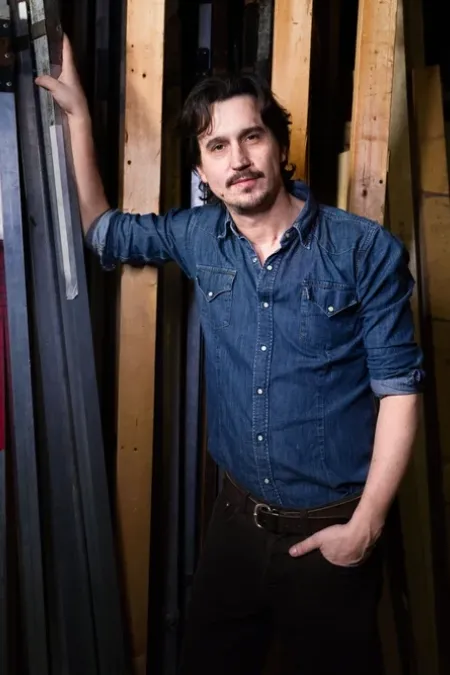 Damiano Michieletto © Stefano Guindani Mann in dunkelblauem Jeanshemd lehnt mit einer Hand an einem Holzrahmen, die andere Hand in der Hosentasche.