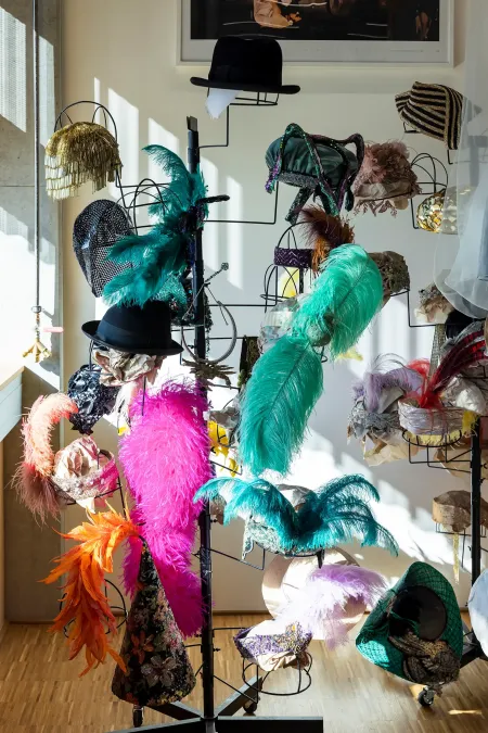 © Bregenzer Festspiele / Kristina Becker Verschiedene bunte Hüte mit großen Federn und Verzierungen auf einem Ständer in einem hellen Raum