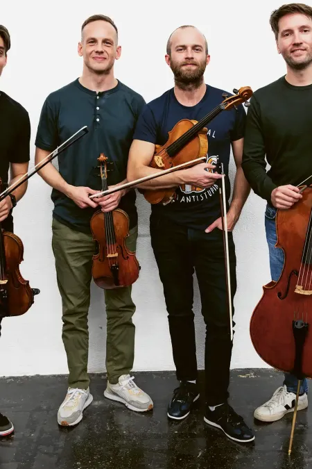 Vier Männer stehen nebeneinander und halten Streichinstrumente, zwei Geigen, eine Bratsche und ein Cello.