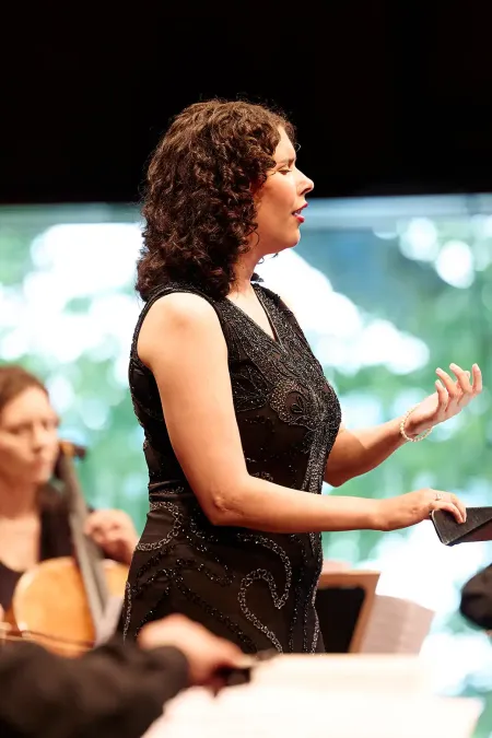 Emma Kajander in schwarzem Kleid steht vor einem Notenpult und singt, im Hintergrund spielen drei Musiker Streichinstrumente.