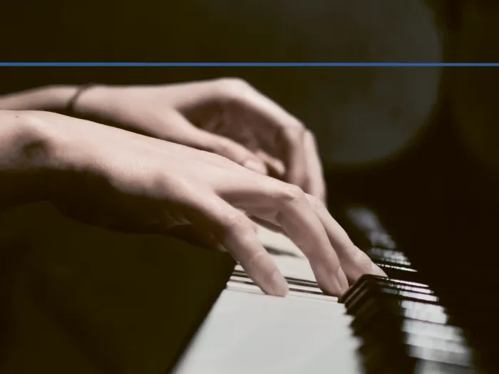 Detailaufnahme von Händen an einem Klavier mit dunklem Hintergrund