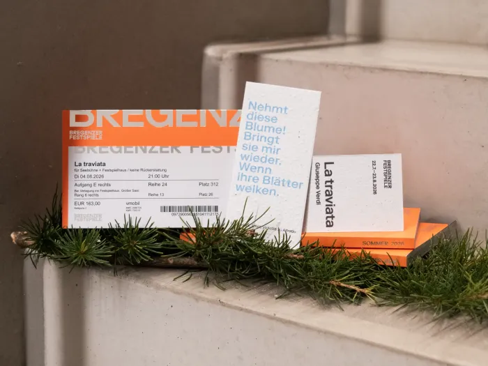 Mehrere Eintrittskarten für die Bregenzer Festspiele 2026 liegen auf einer Treppenstufe, davor Tannenzweige. Eine Karte trägt den Titel 'La traviata'.
