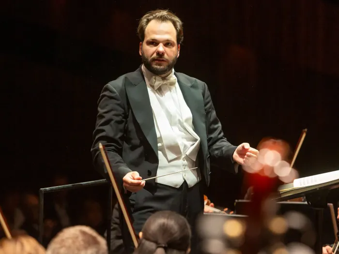 Dirigent in Frack steht vor Orchester und hebt den Taktstock