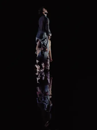 Zwei Tänzer:innen in einer modernen Tanzpose auf dunklem Hintergrund mit Spiegelung am Boden