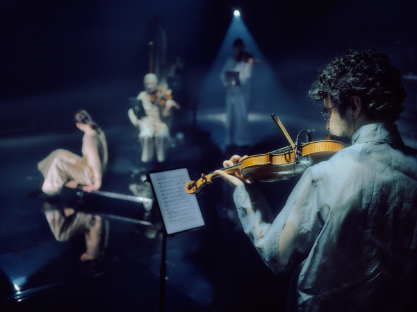 Geiger spielt auf einer Bühne mit drei weiteren Musikern in gedämpftem Licht