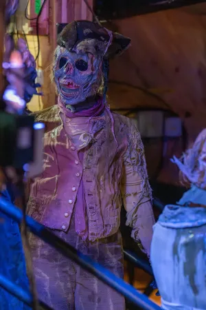 Person in zerlumpter Kleidung und Hut steht in einem dunklen, backstage Bereich mit Holzwänden