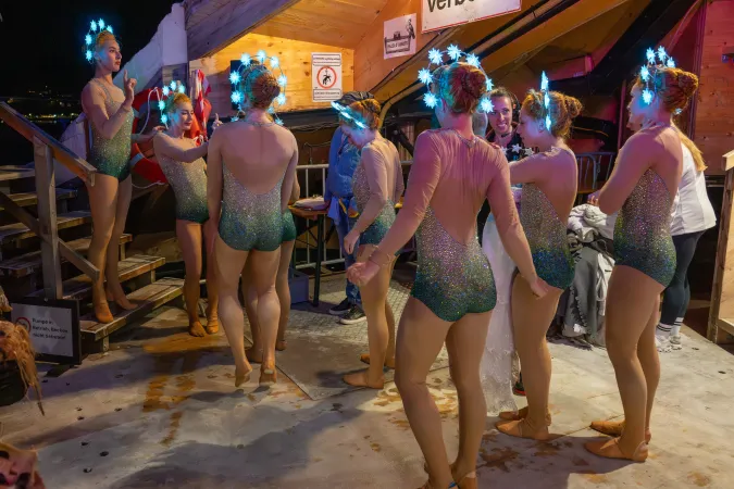 Tänzerinnen in glitzernden Kostümen mit leuchtenden Sternen auf dem Kopf backstage vor einer Holzhütte