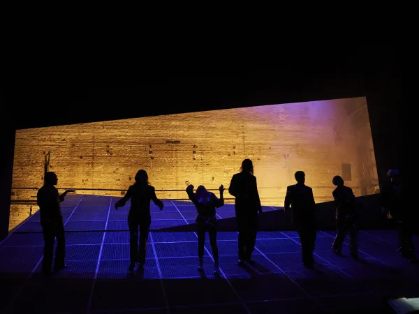 Sechs Personen silhouetten vor einer großen, schräg stehenden Wand mit goldener Textur bei den Bregenzer Festspielen