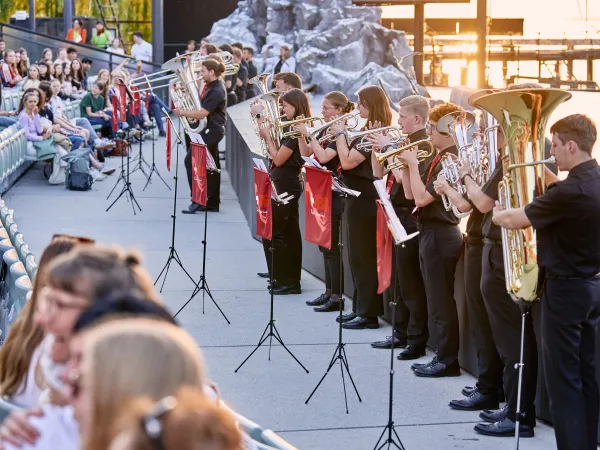 Jugendblasorchester spielt im Freien vor Publikum, Musiker:innen in schwarzer Kleidung mit Blechblasinstrumenten