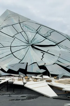 Nahaufnahme einer großen, kreisförmig zersprungenen Glasscheibe mit vielen Rissen und abgebrochenen Stücken