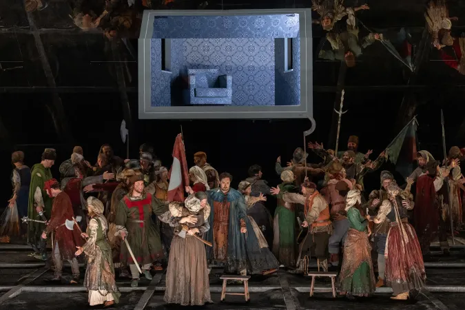 Bühnenbild mit vielen Schauspielern in historischen Kostümen vor einer großen Leinwand, die ein blau gemustertes Zimmer mit Sessel zeigt