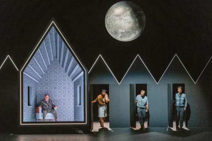 Vier Männer stehen oder sitzen vor einer Kulisse mit geometrischen Formen und einem großen Mond im Hintergrund