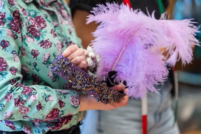 © Bregenzer Festspiele / Kristina Becker Person hält eine mit Perlen und Stickereien verzierte violette Maske mit großen lilafarbenen Federn