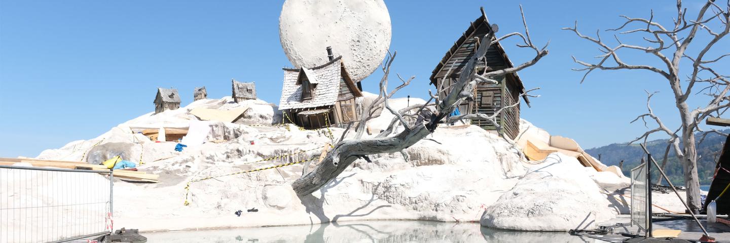 Ausschnitt Bühnenbild "Der Freischütz"  mit Mond, Schneehügel mit Häuschen und Wasesr